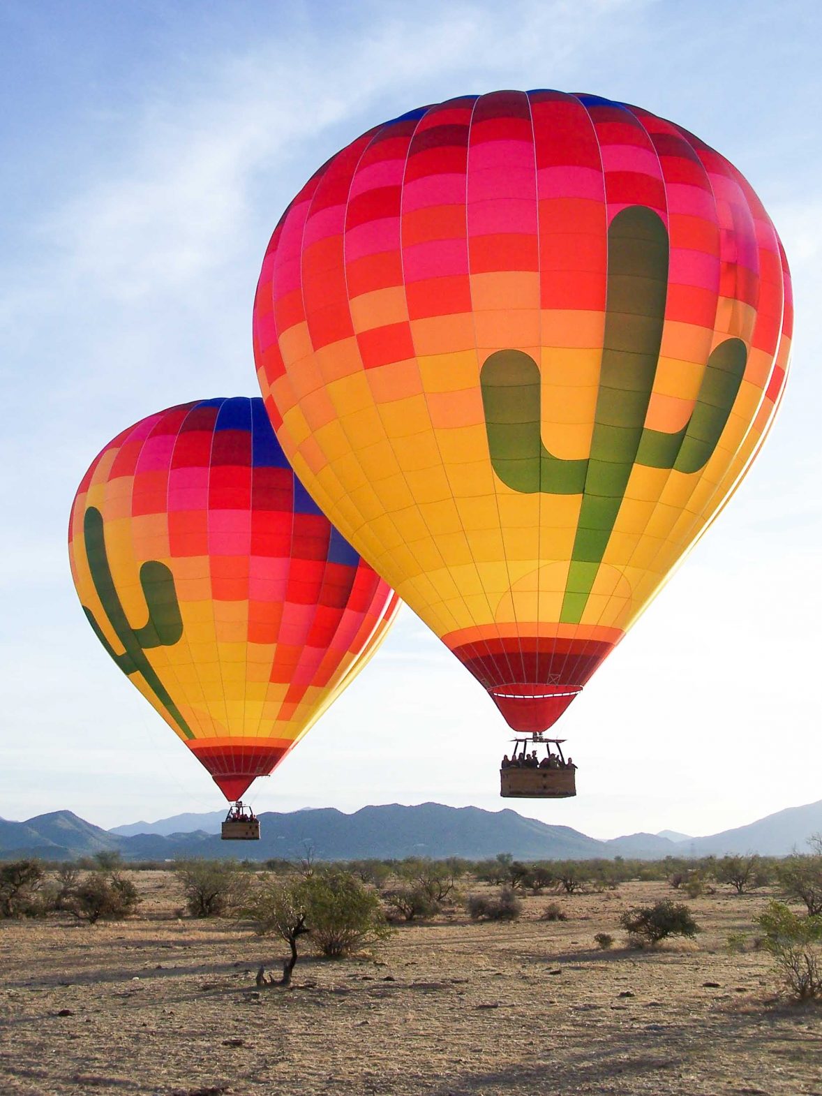 Two hot air balloons fly above a dry landscape.