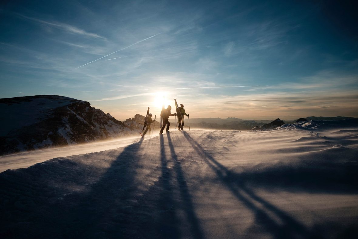 A group of skiiers walk up a mountain in low light.