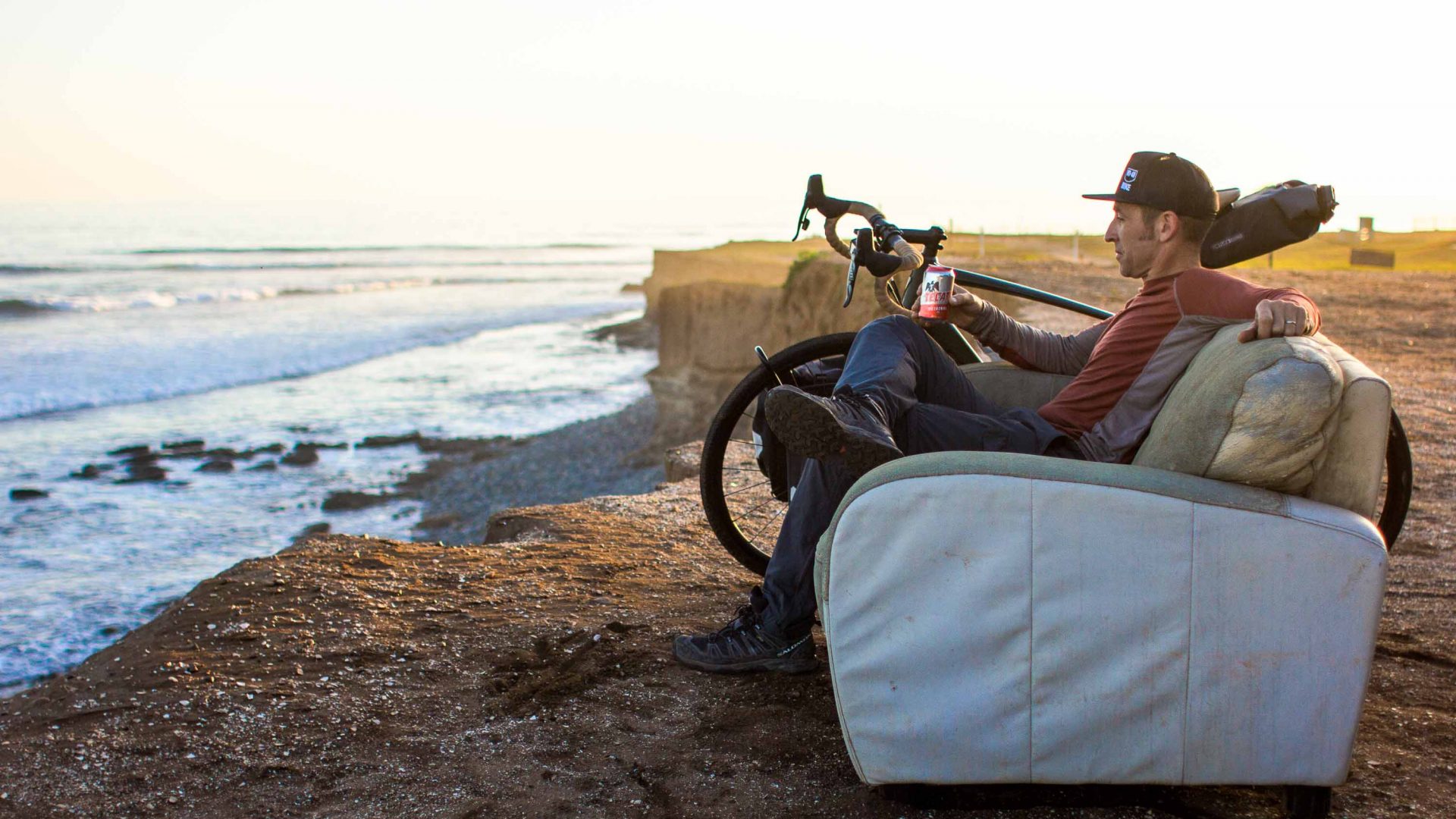 A man sits on a couch overlooking the ocean with his bicycle.
