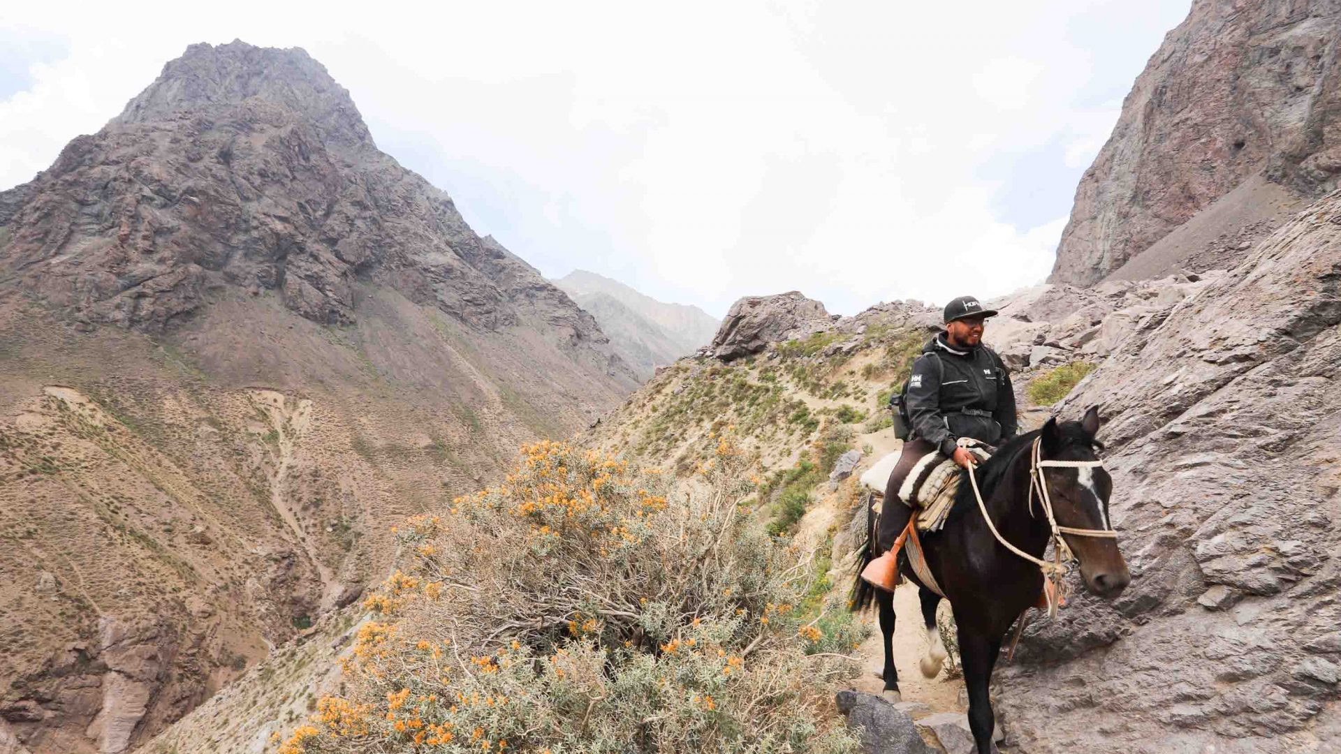 A man rides his horse through the arid mountains.