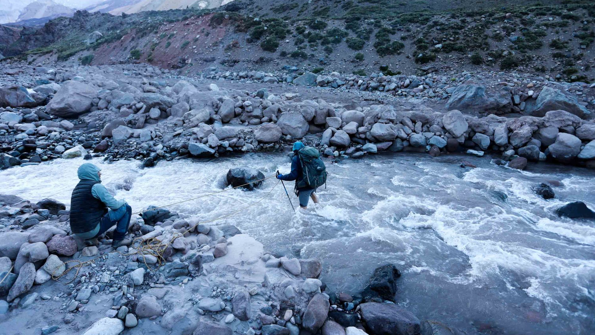 A hiker crosses a stream wearing his backpack.
