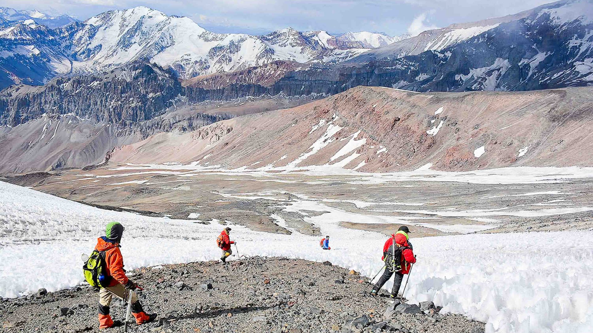 Three hikers in orange stand and look at a glacier.