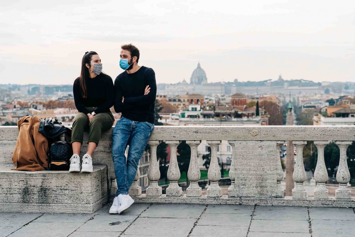 A couple in masks sit overlooking Rome, Italy.