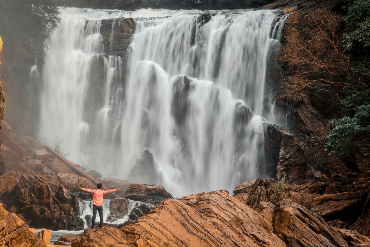 A man stands with his arms wide open at some falls.