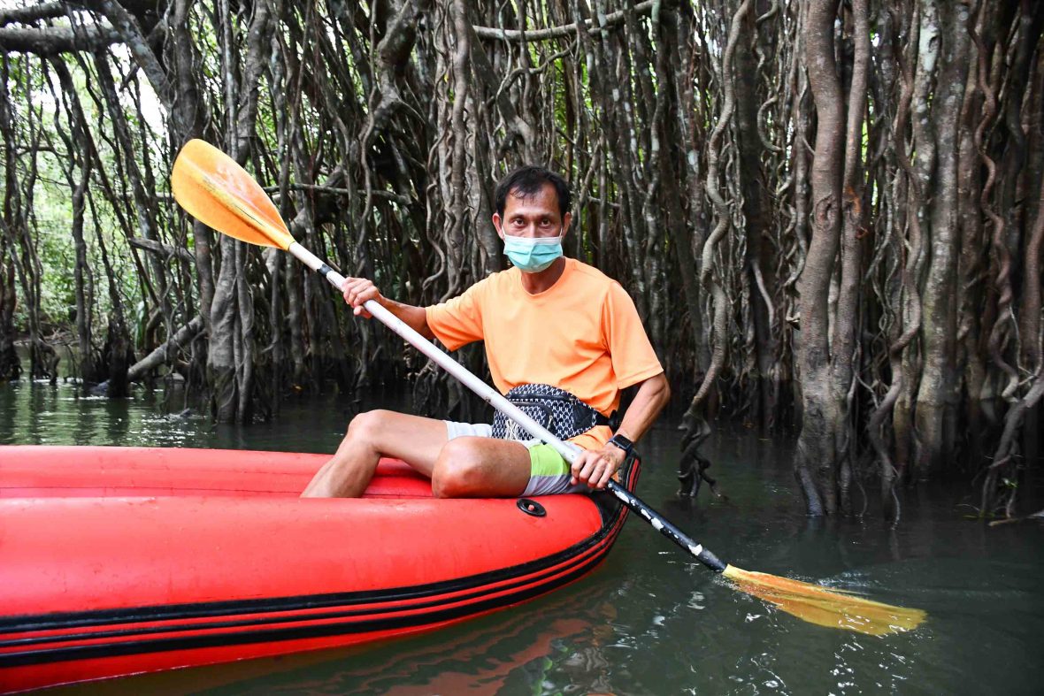 A man in a face mask kayaks in front of some mangroves.