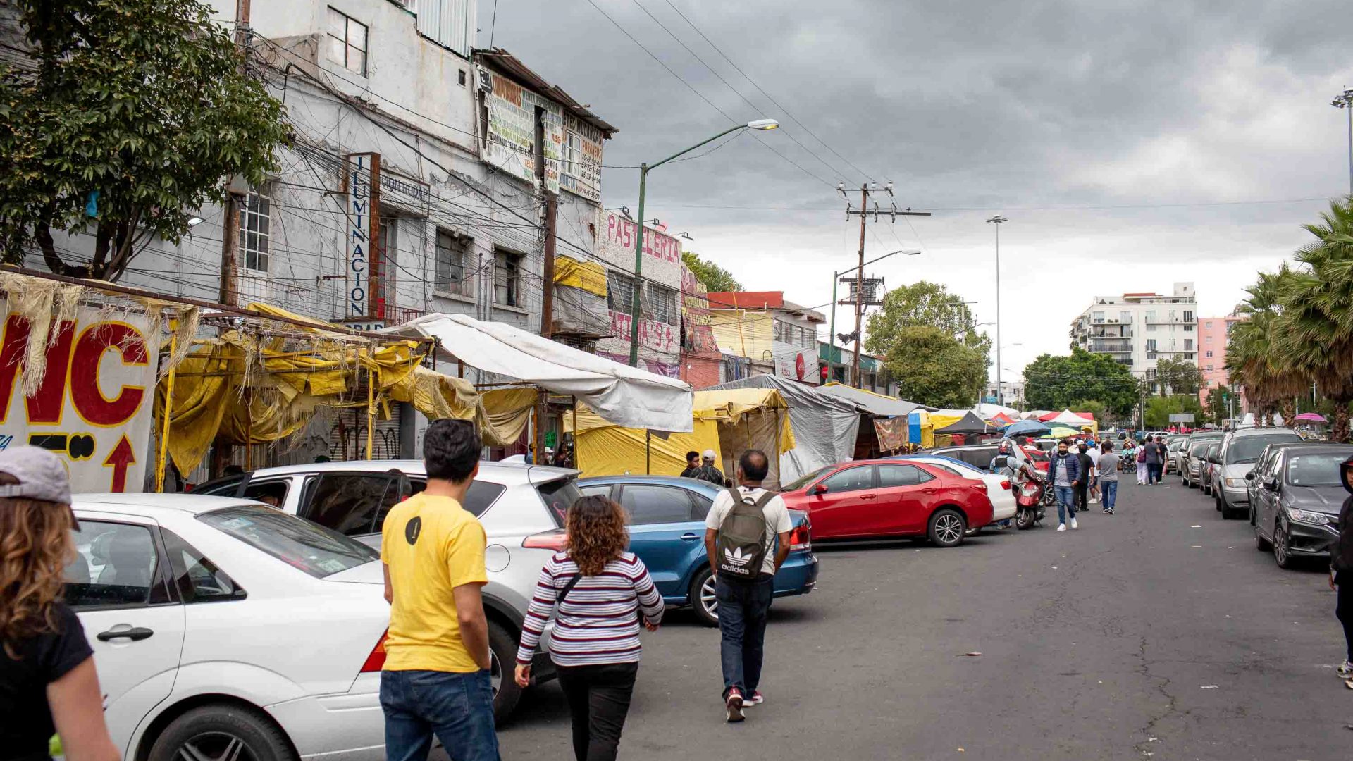 The street outside of the Tepito market show stalls, cars and people walking.