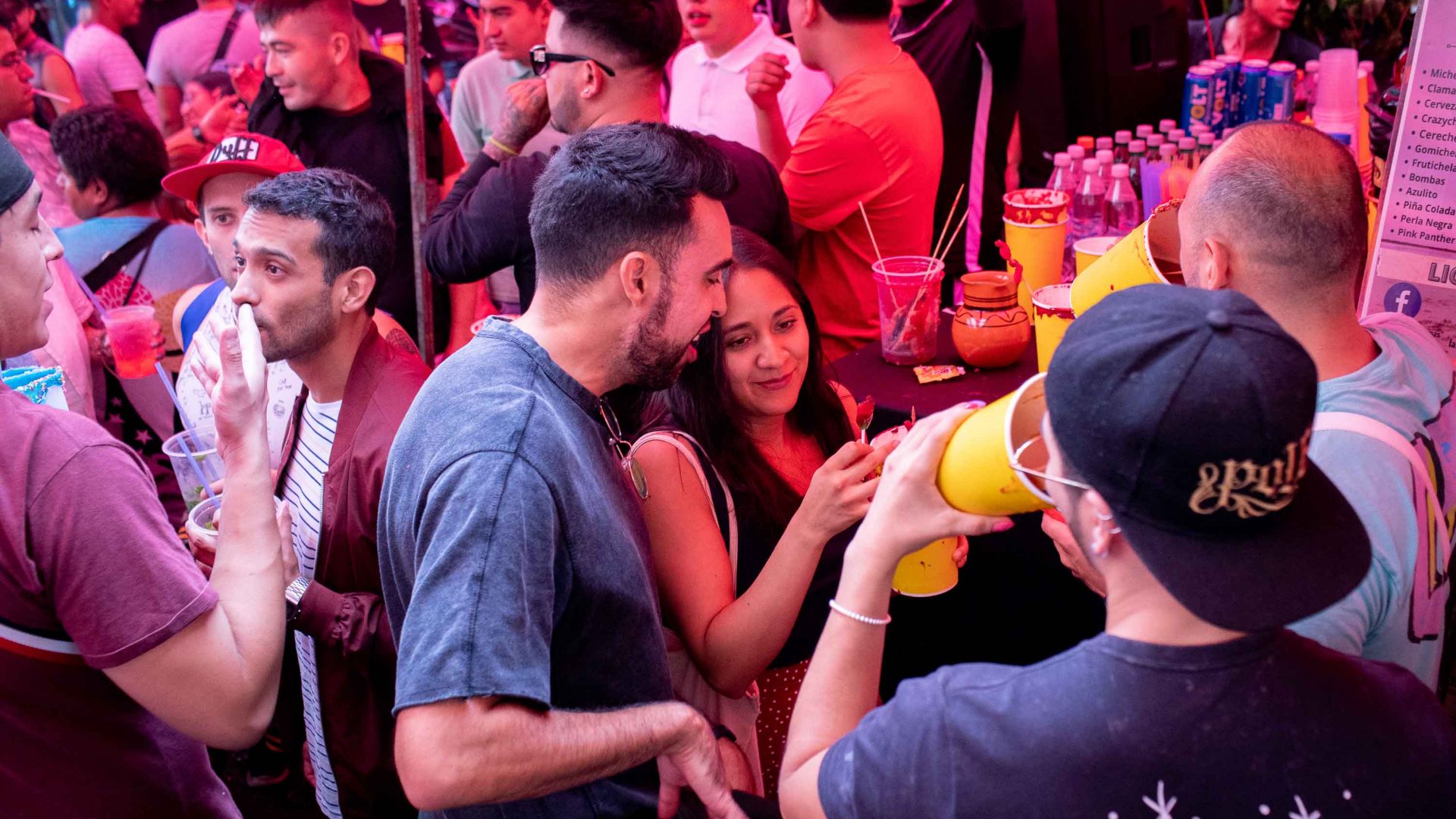 A group of people stand together drinking micheladas.
