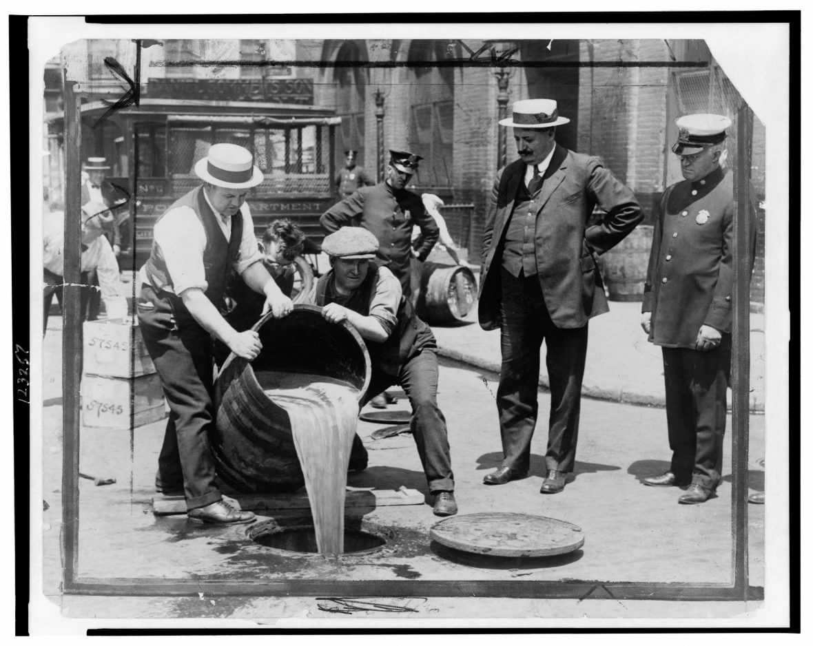 New York City Deputy Police Commissioner watching agents pour liquor into sewer.
