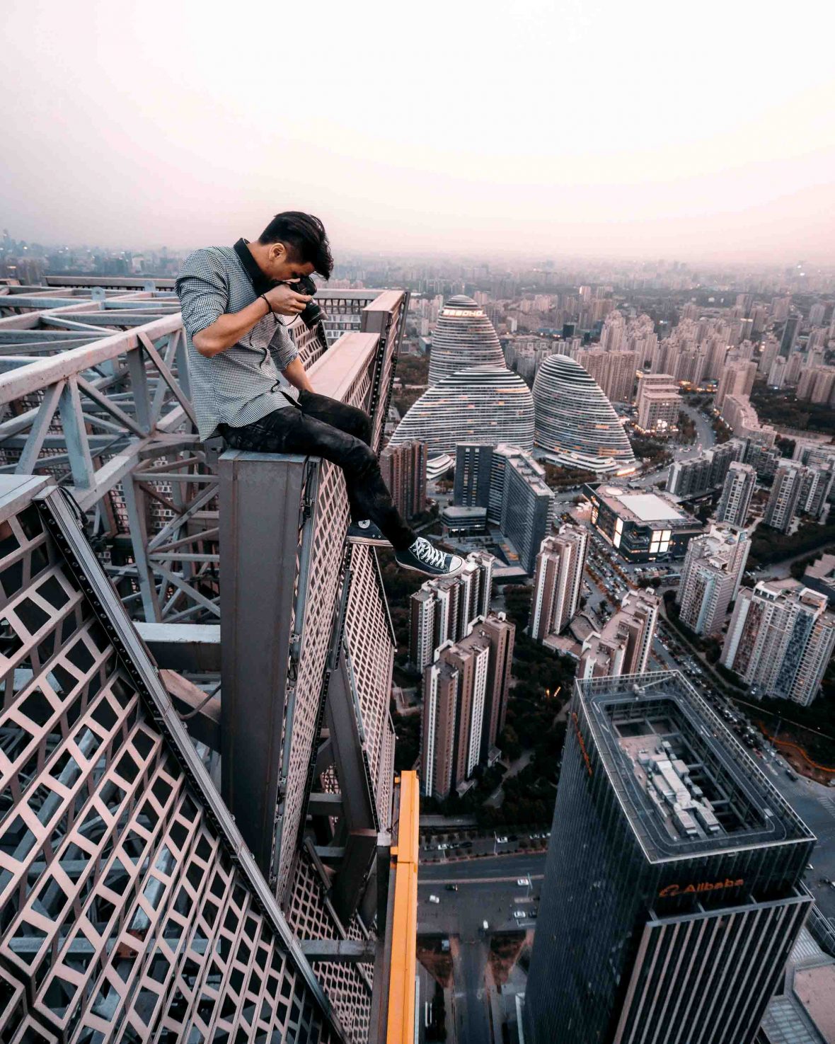 A man takes a photo from the edge of a highrise building.