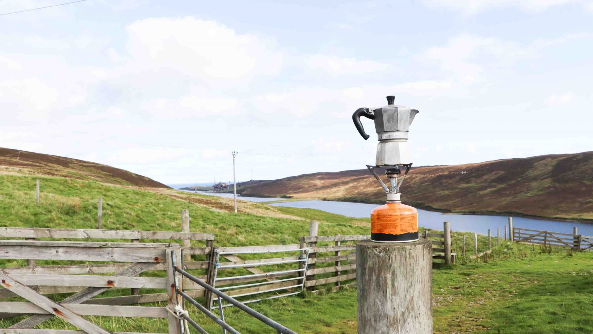 A coffee pot on a camping stove, atop a fence post.