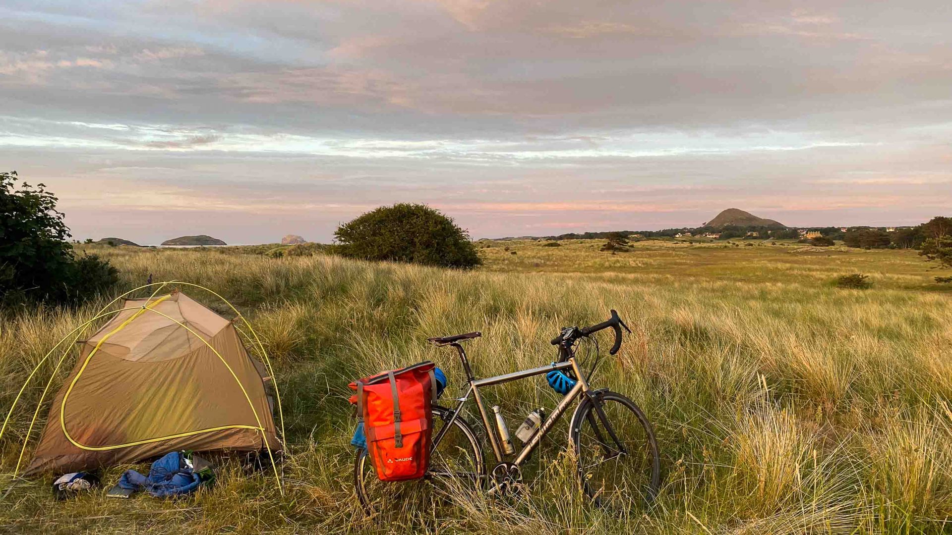 A tent and bike in a field at sunset.