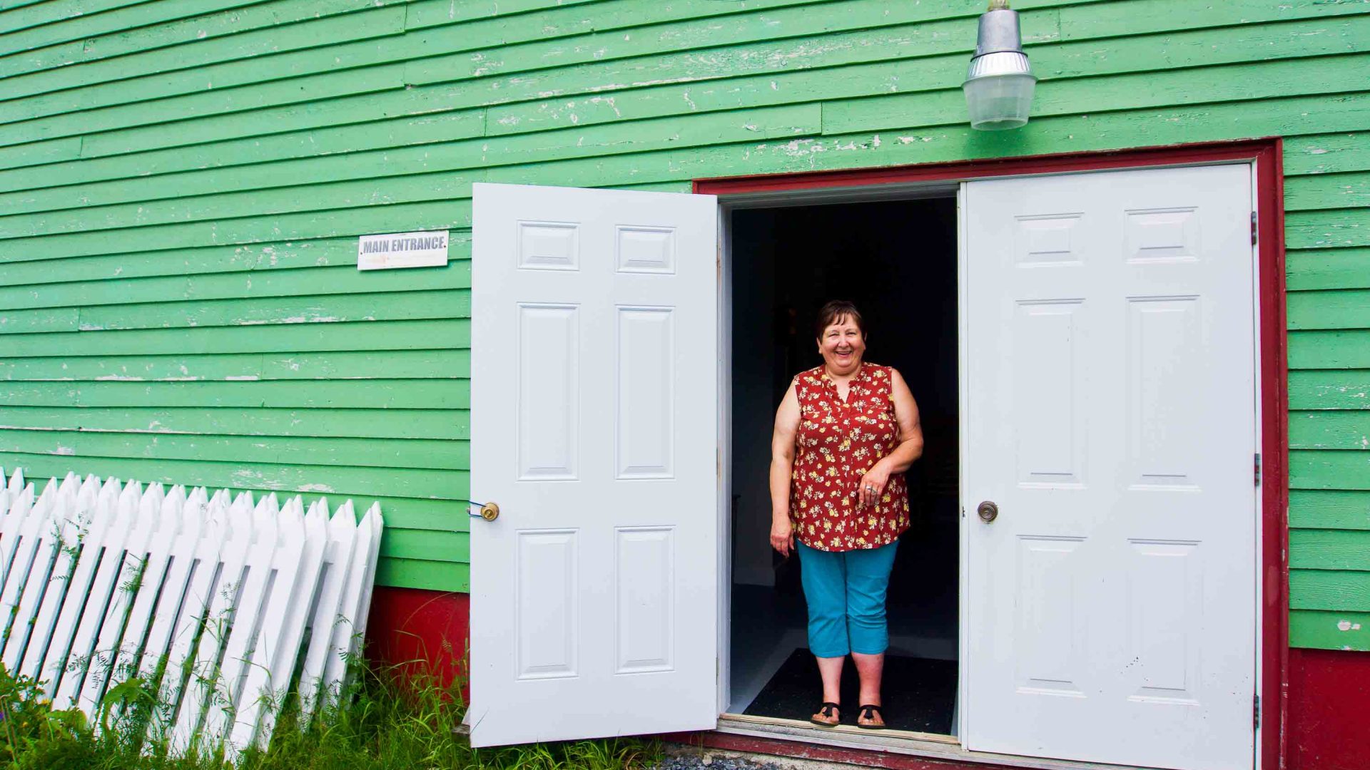 A woman smiles in the doorway of a green building.