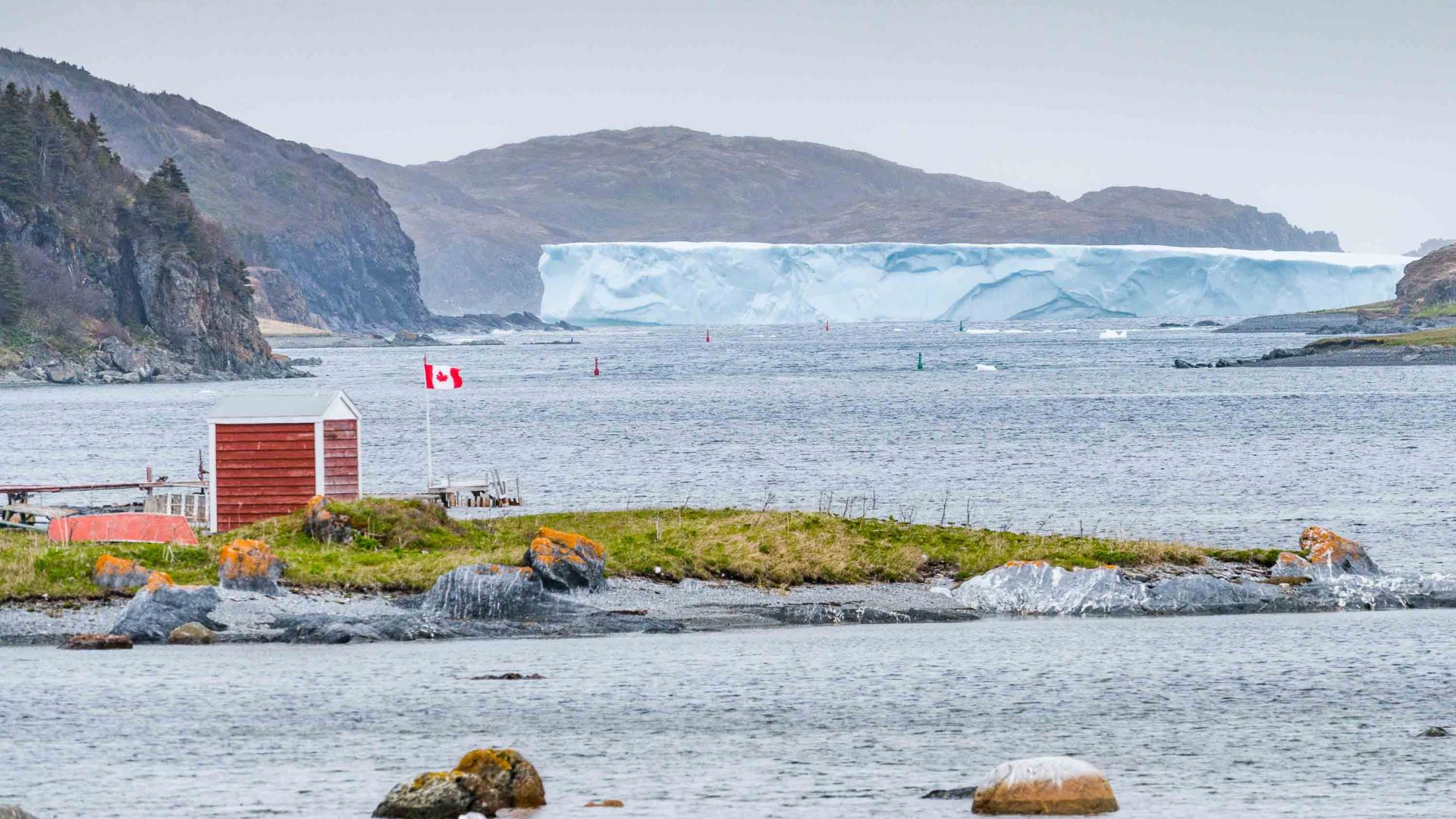 An iceberg is visble in the background while a red and white hut is in the foreground.