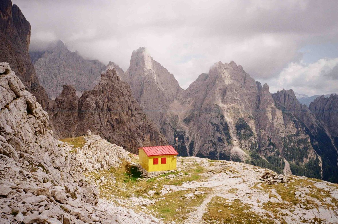 A yellow hut surrounded by mountains.
