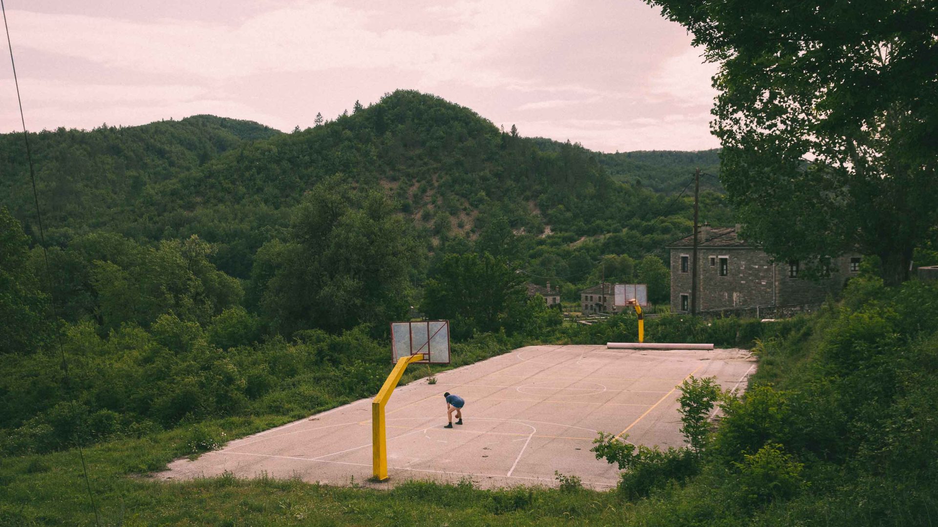 A lone person plays on a basketball court surrounded by hills.