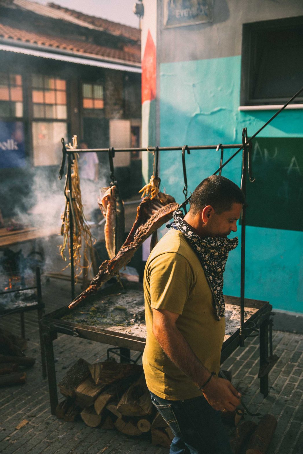 A man walks past some meat that is roasting outdoors.
