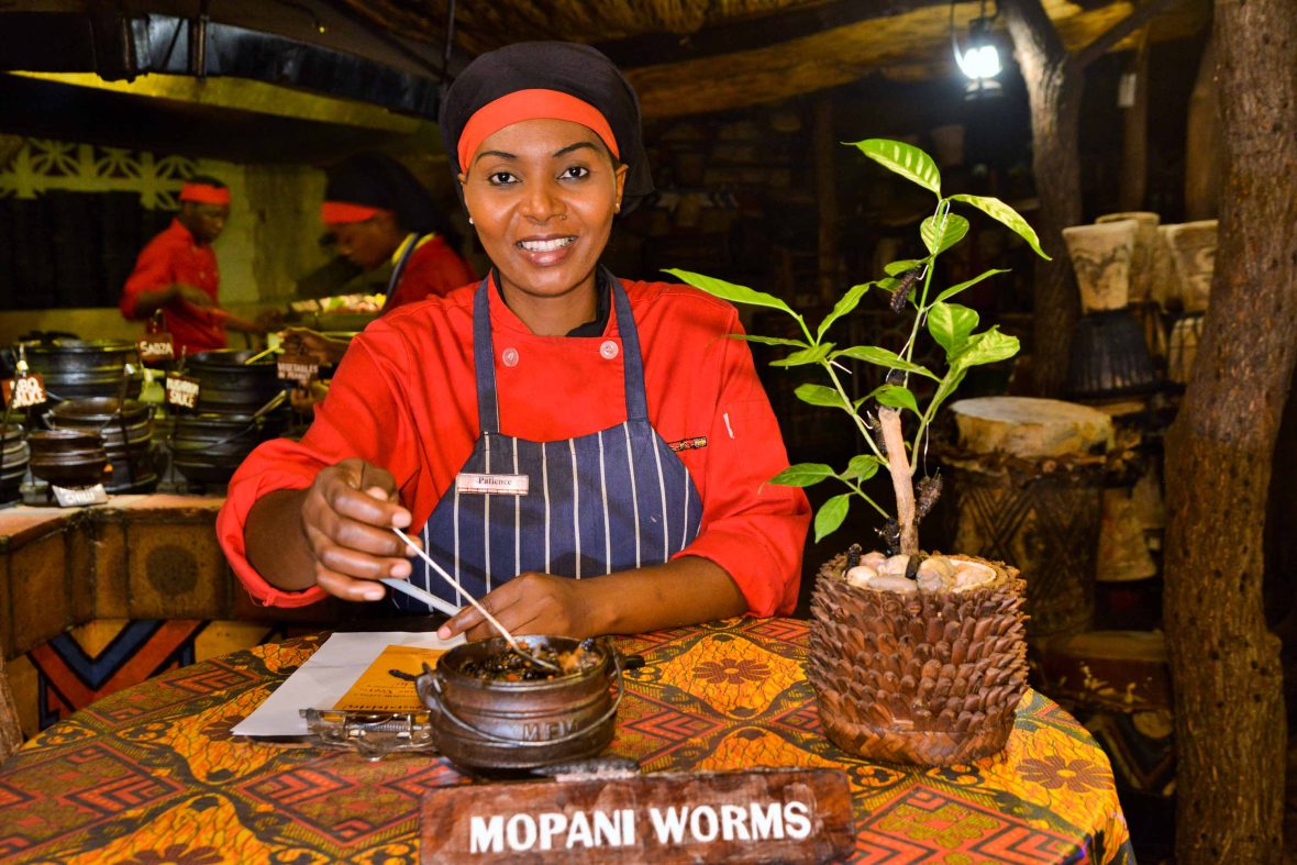A woman smiles in front of a jar of worms.