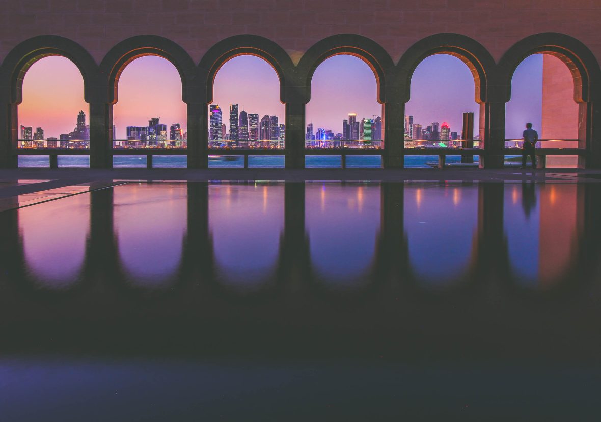 The city of Doha is seen at dusk through the arches at a museum.