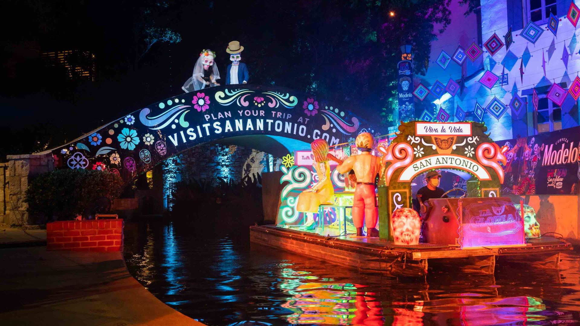A colorful boat with many lights, floats past a bridge.