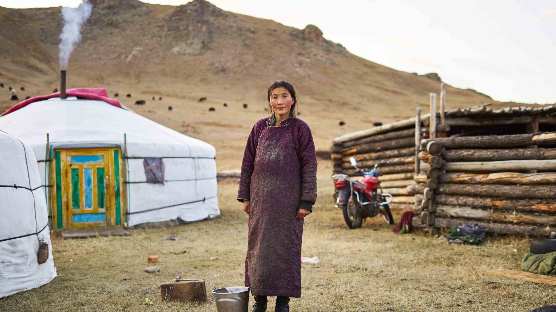 A woman stands out the front of some yurts and looks at the camera.