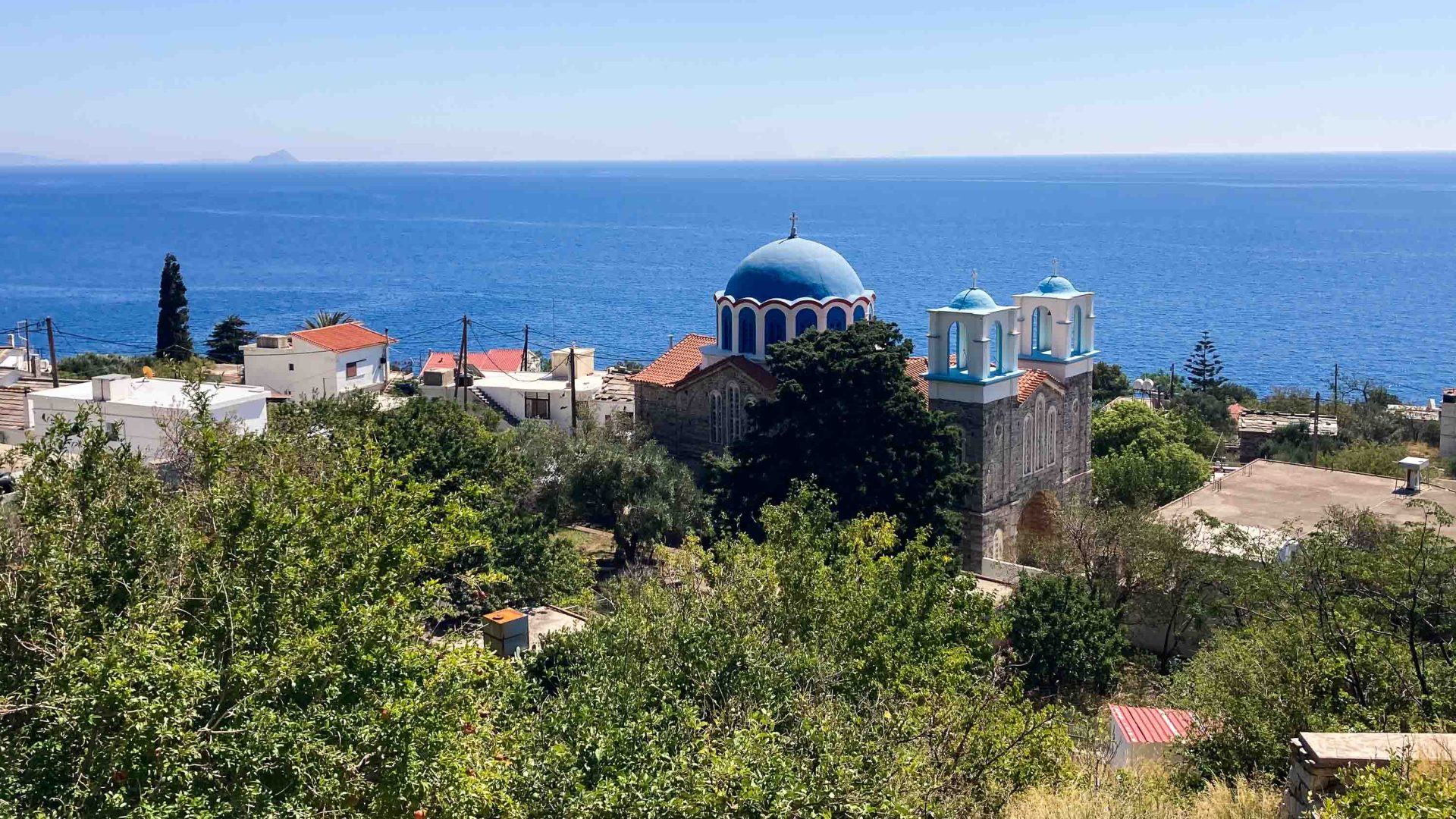 The blue dome of a church stands above other houses, backed by sea.