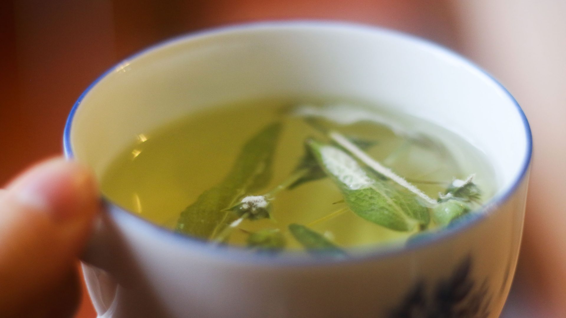A cup of yellow looking tea with leaves in it.