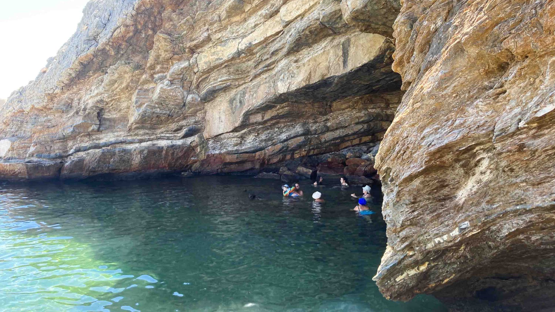 People paddle through blue water under a cave.