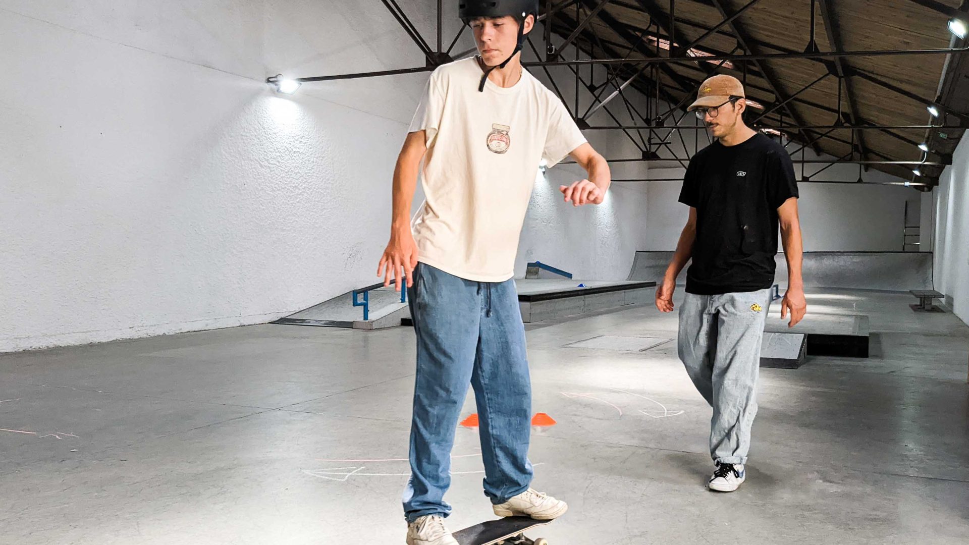 A young teenager learns to skate, watched on by his instructor.