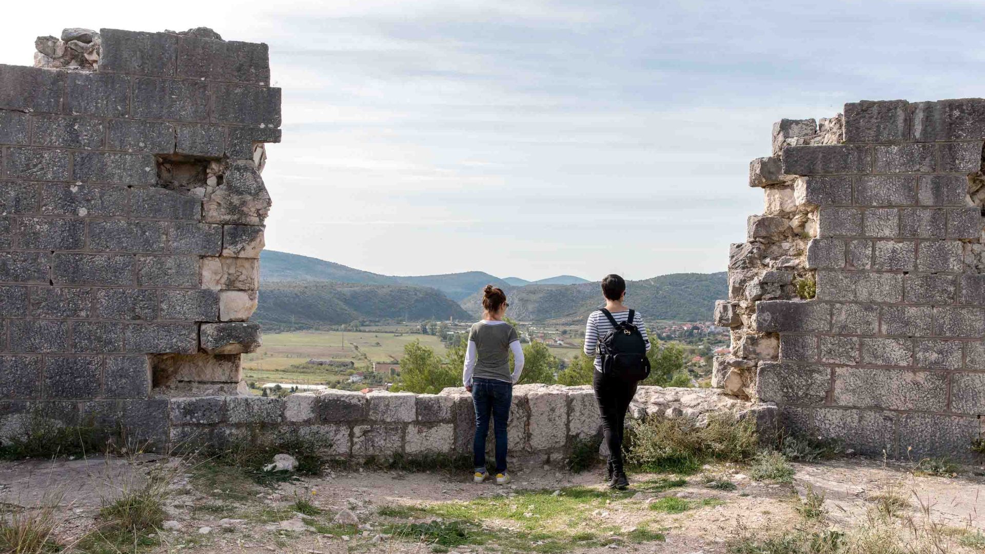 Two people look out at a view from between some ruins.