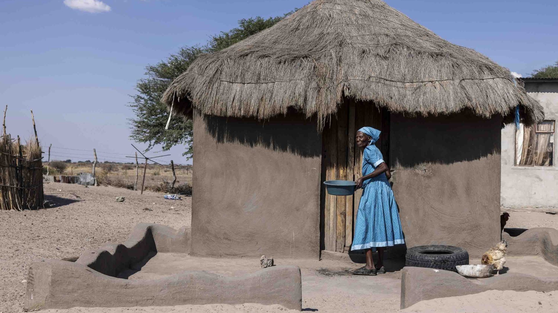 A woman in blue outside of her hut.