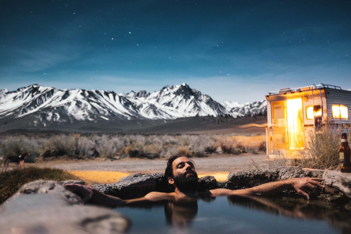 A man soaks in a hot spring, backed by snowy mountains.