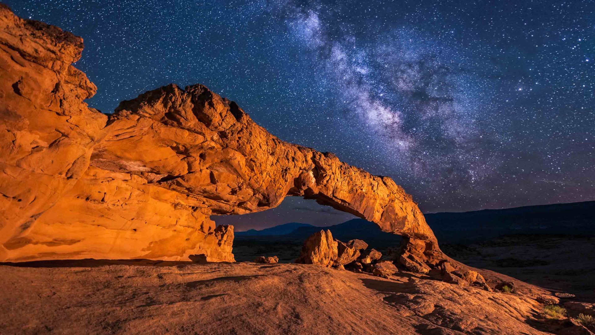 The natural arch of a rock is illuminated by the night sky.