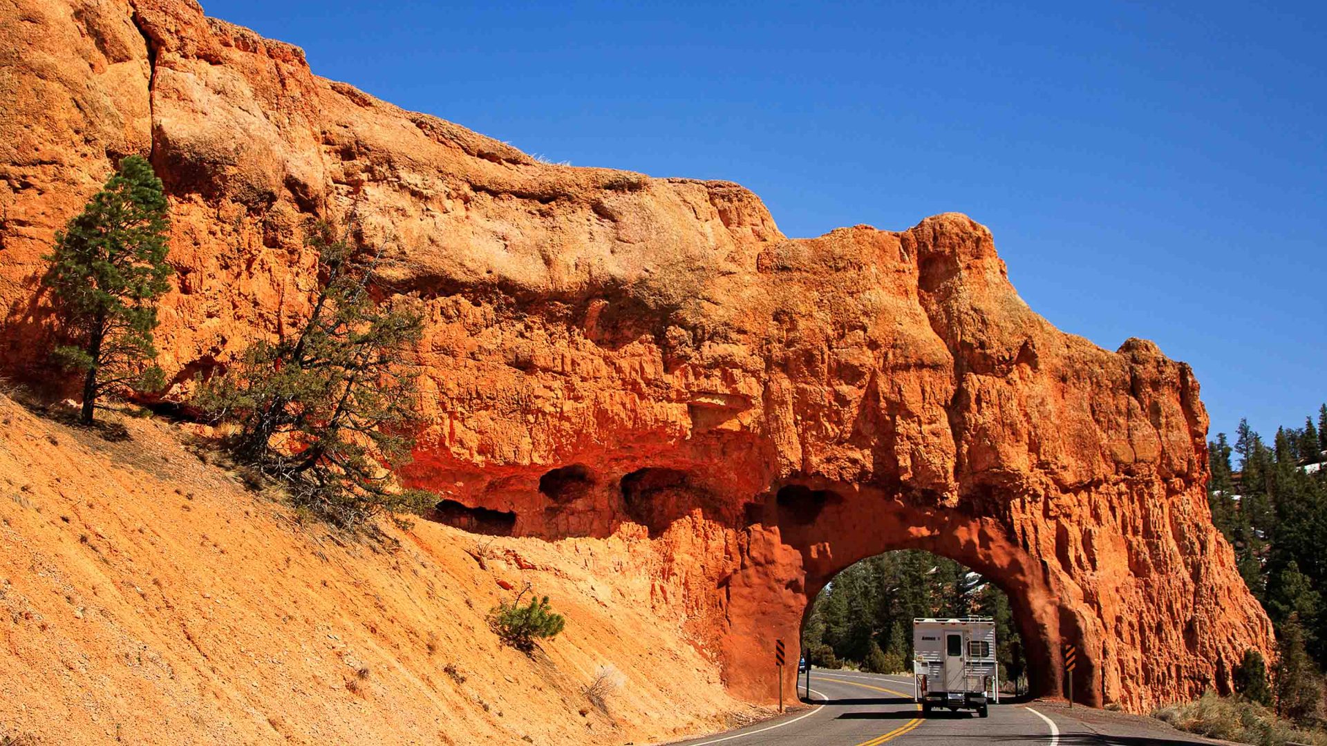 A car passes under a rock arch over the road.
