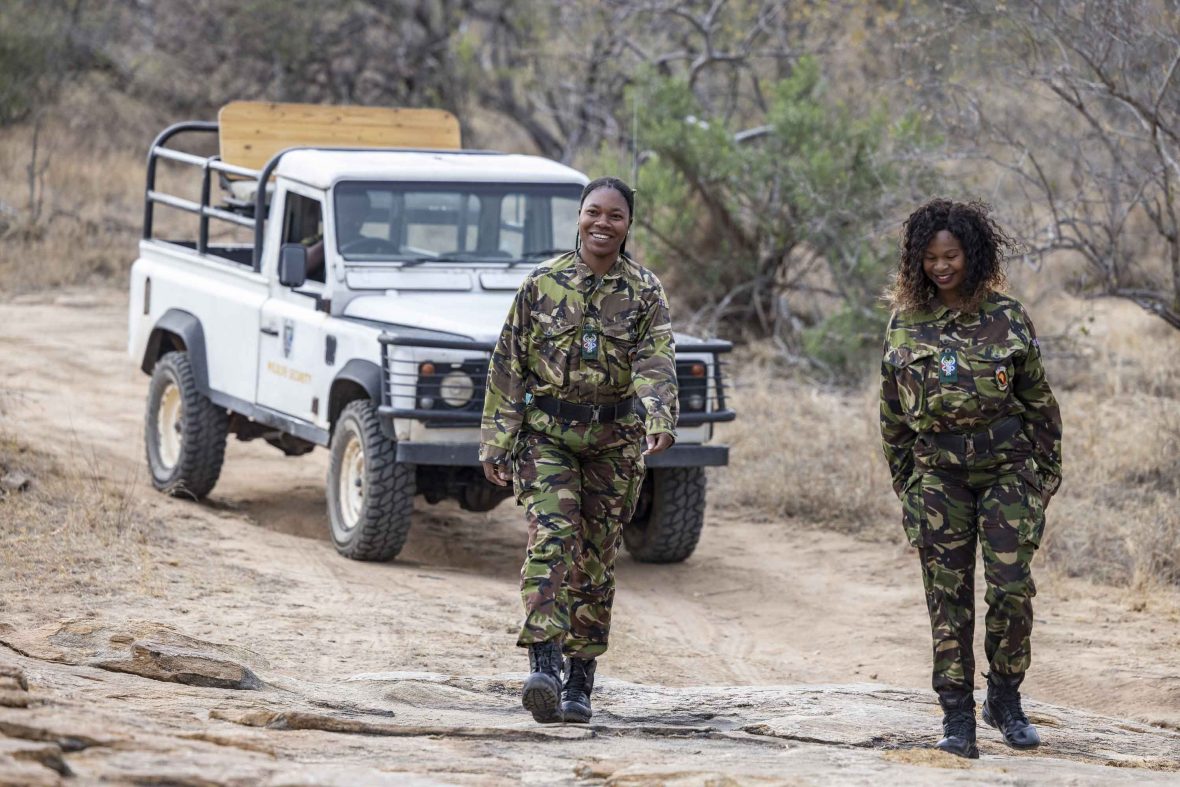 Two female mambas walk smiling away from their jeep.