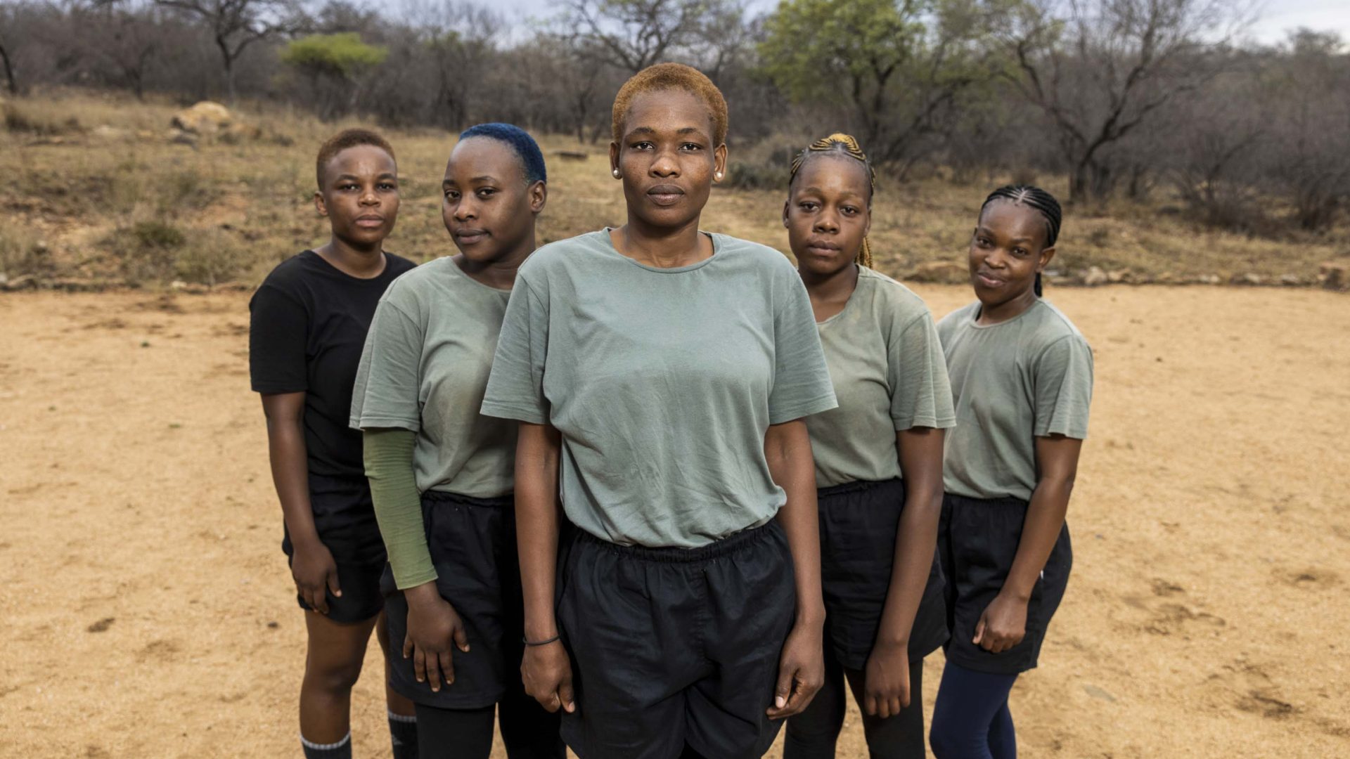 A group of young women in formation look straight to camera.