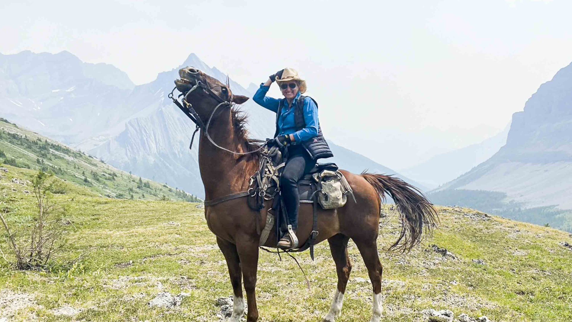 A woman on a brown horse with mountains in the background.