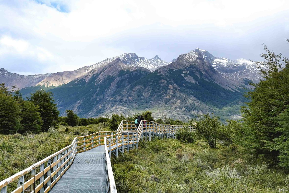 A boardwalk through a national park with tall mountains.