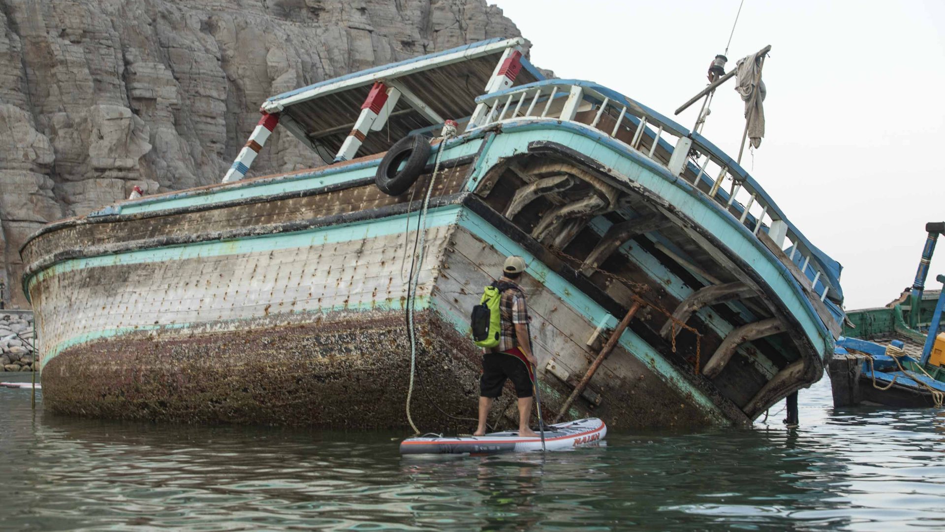 A paddle boarder looks at the wreck of a boat.