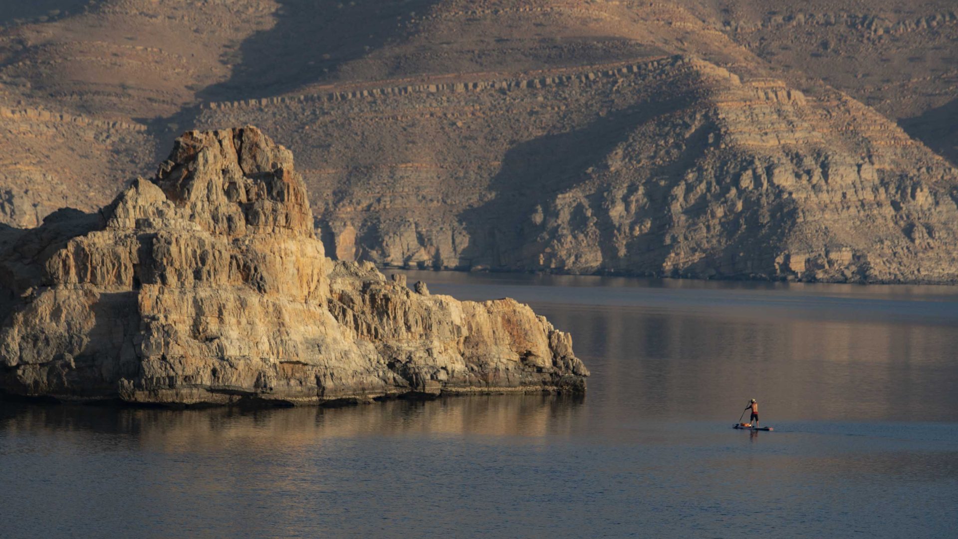 A lone person on a paddle board surrounded by desert fjords.