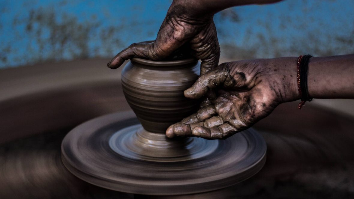 Two hands handling clay around a pottery wheel.