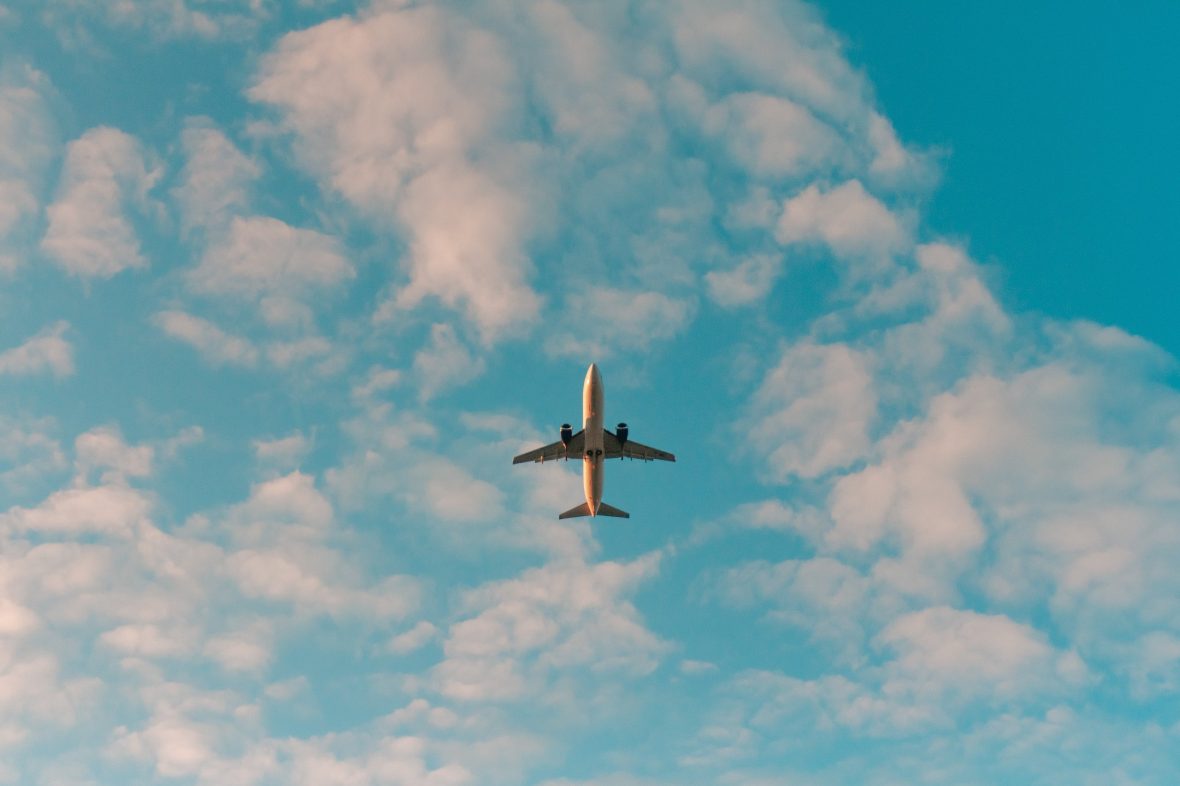 An image of a plane in the middle of the image surrounded by clouds and a blue sky