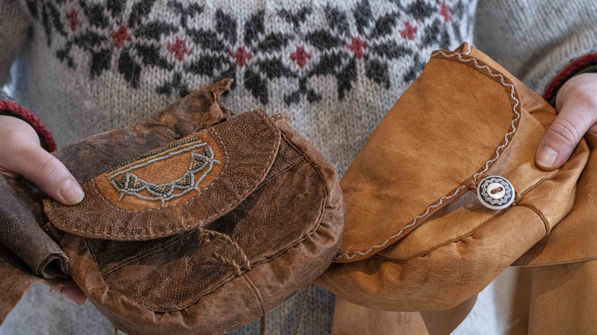 Hands holding two traditional Sápmi bags made from reindeer leather.