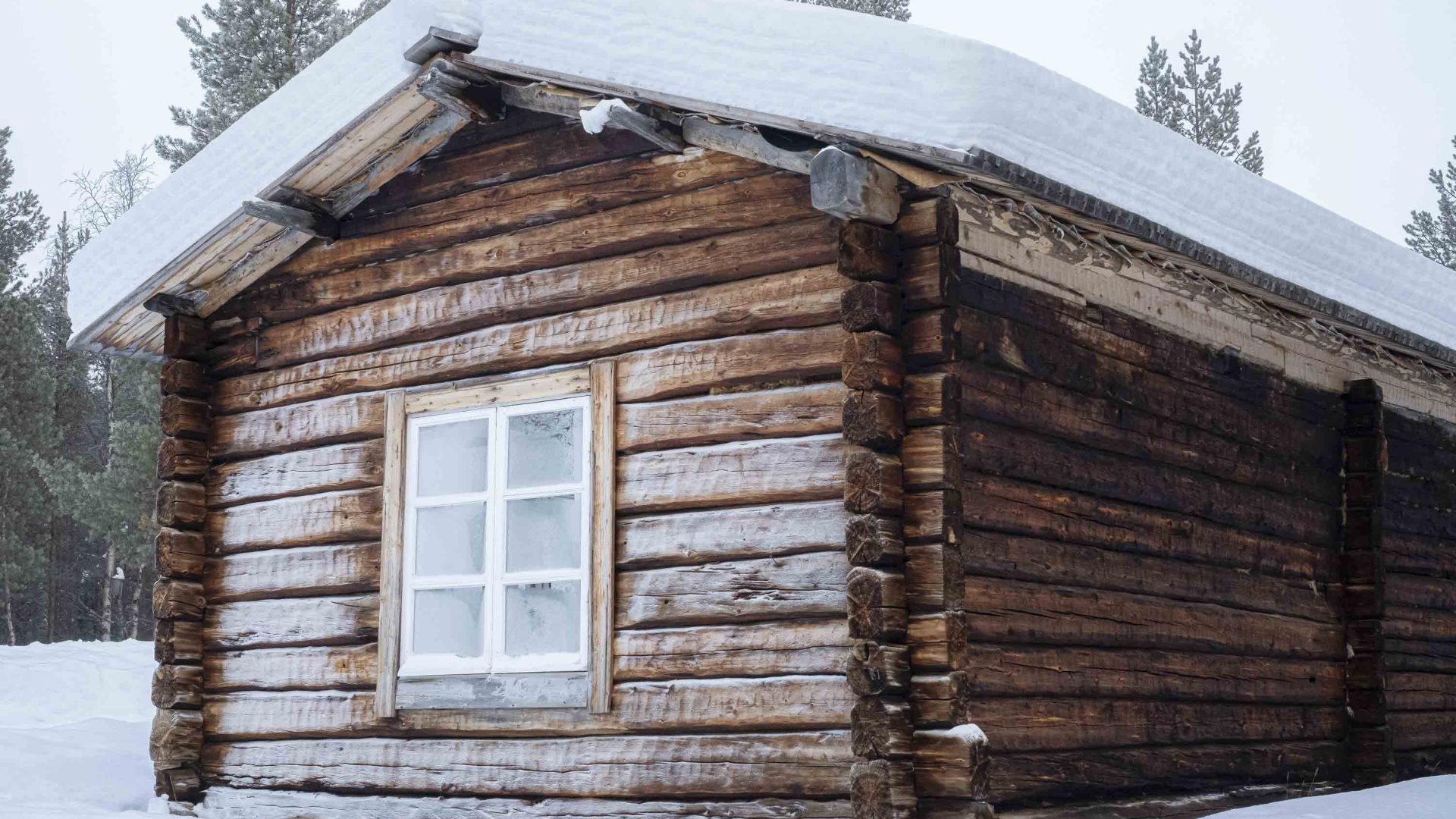 A snow-topped wooden homestead against a snowy background.