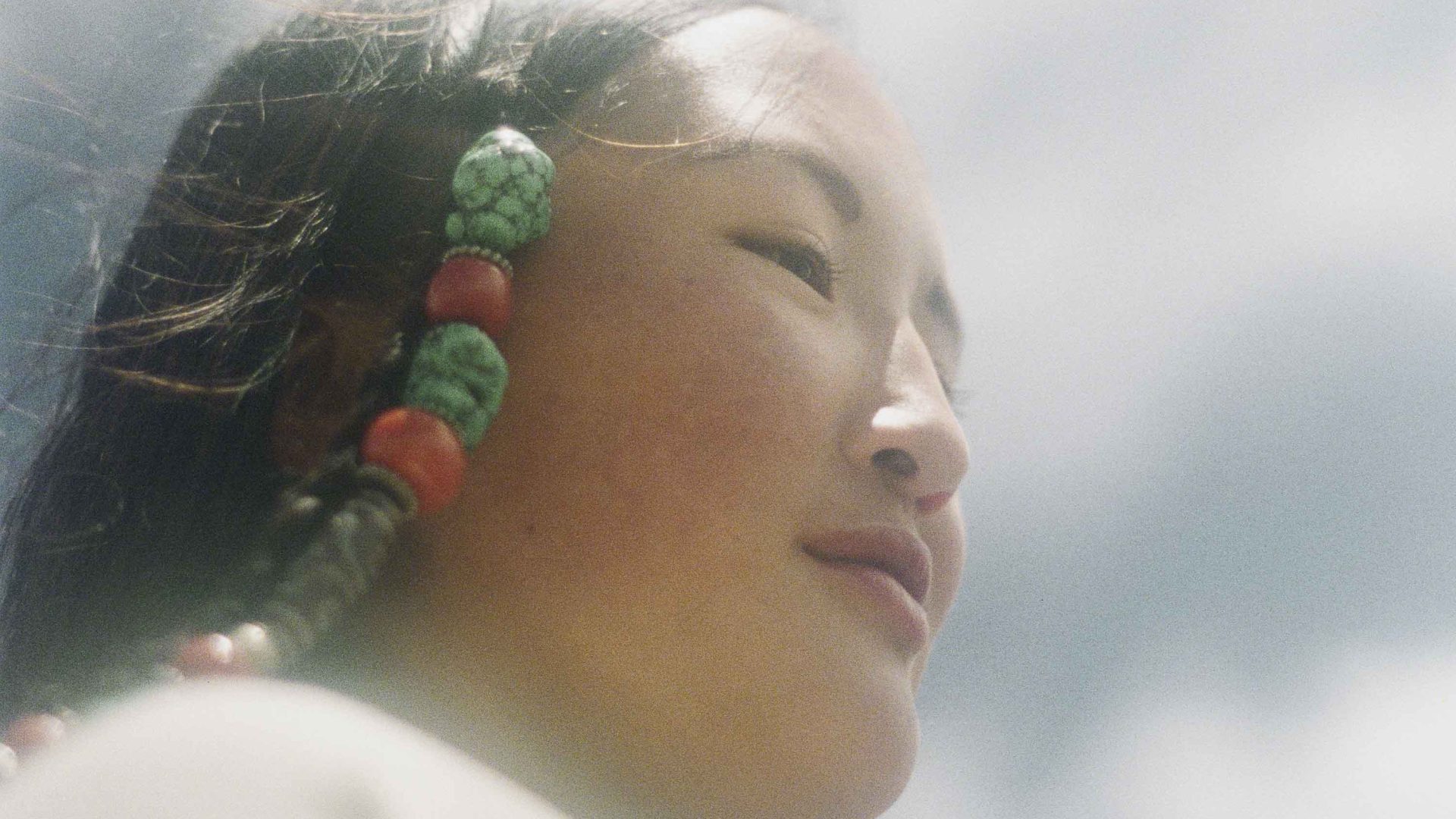 A close up of a young girls face. She has red and green beads in her hair.
