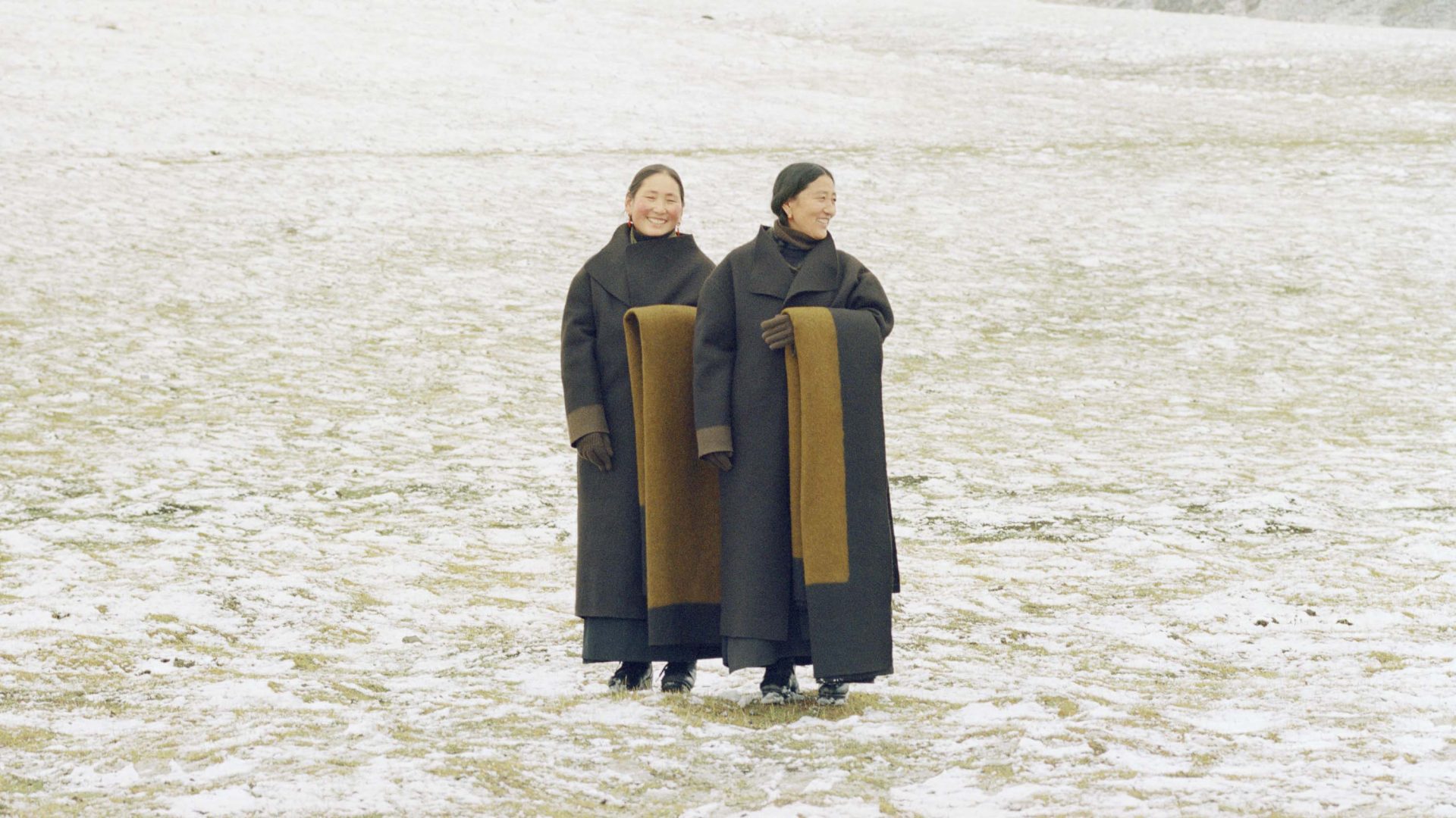 Two women wearing traditional textiles, standing in snow.