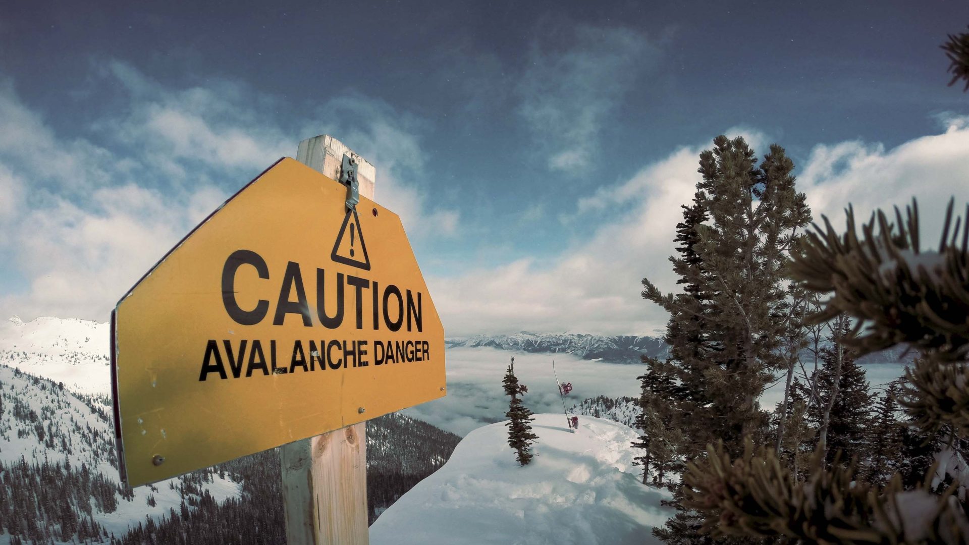 A sign warning of avalanche on a snowy mountain.