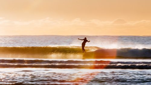 Belinda Baggs surfing on a longboard at sunset.