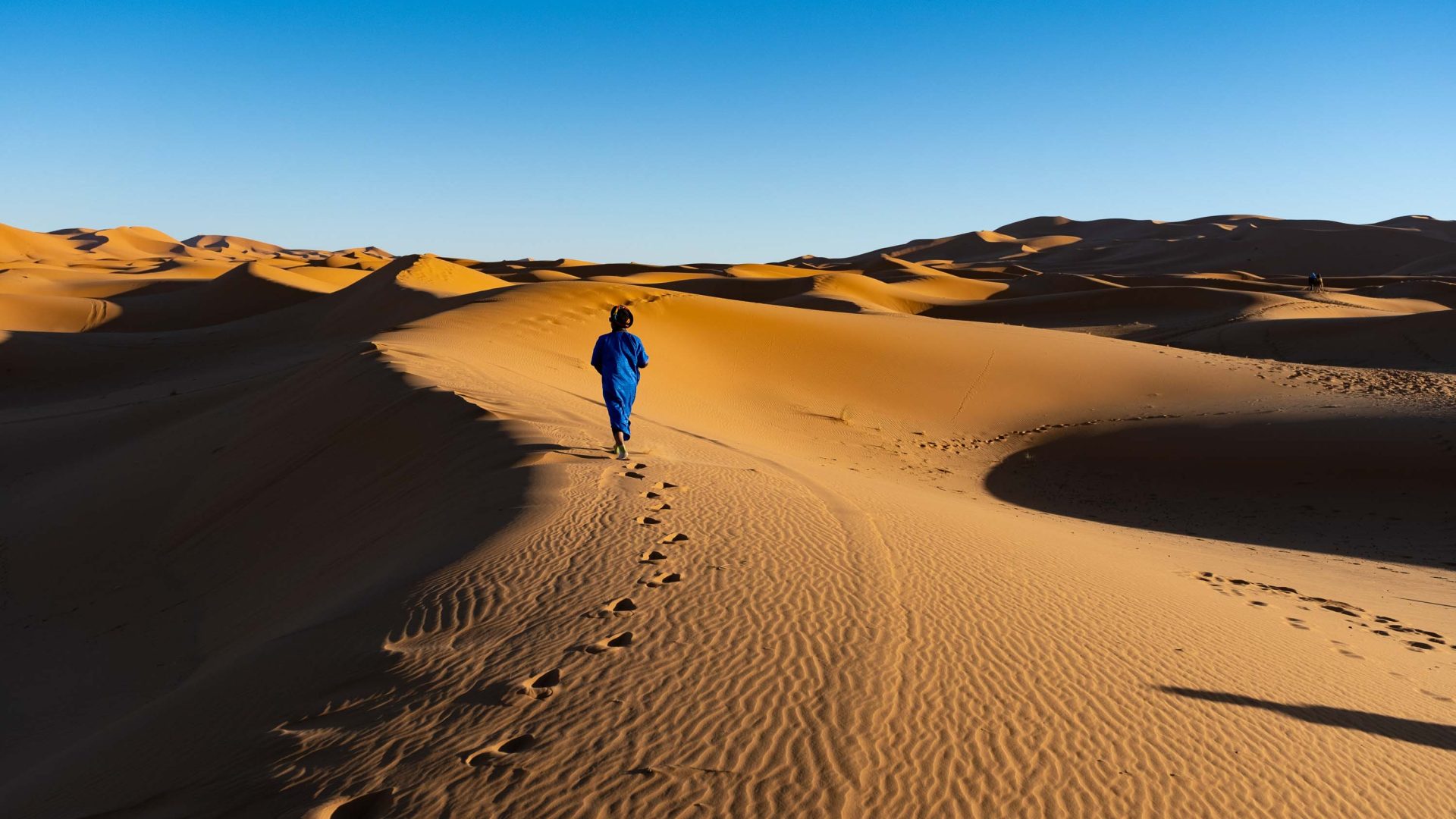 A man in blue walks through the desert.