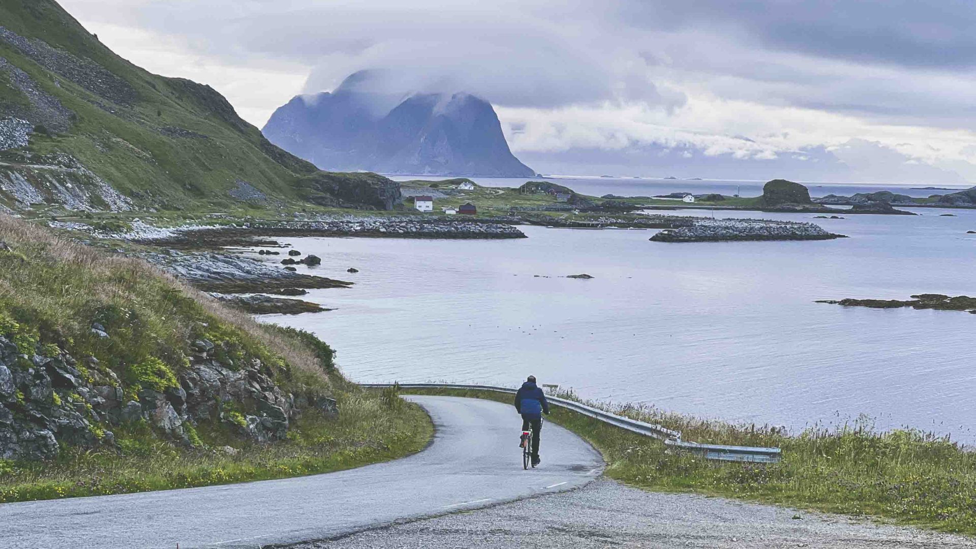A person cycles down a road that has cliffs jutting out of the water below.