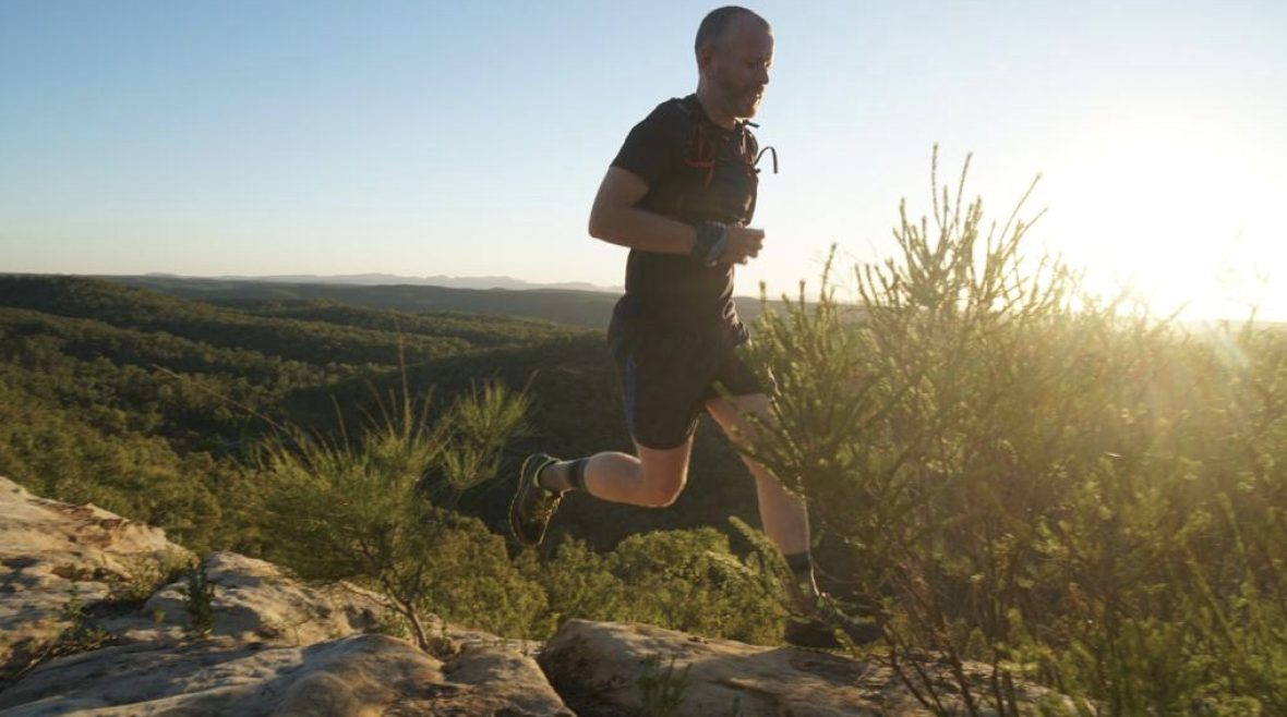 A man trail-running at sunset, silhouetted by the golden light